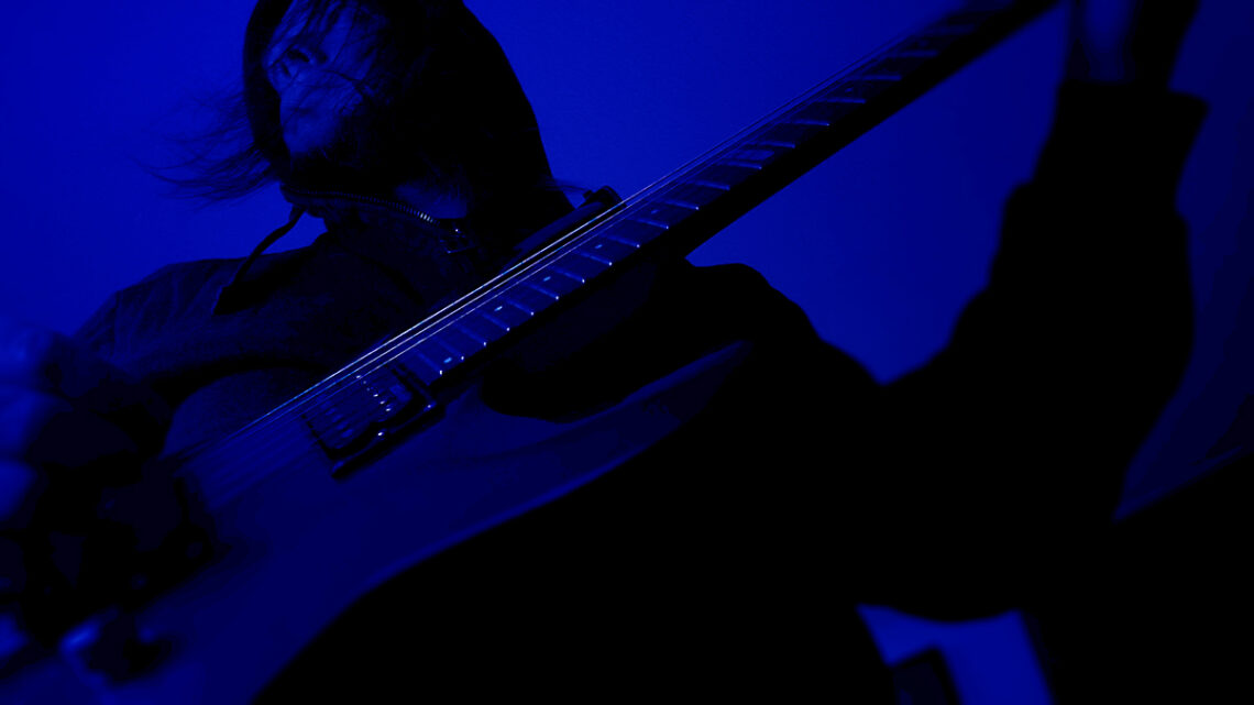 T. M. Mäkelä playing electric guitar in deep blue light